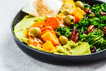 Wall Mural - Avocado hummus with baked vegetables, olives, nuts and berries in black plate. Healthy vegan food concept.