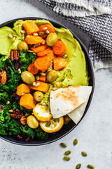 Wall Mural - Avocado hummus with baked vegetables, olives, nuts and berries in black plate, top view. Healthy vegan food concept.