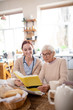 © zinkevych - Nurse sitting near pensioner reading book in the morning