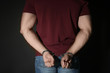 © New Africa - Male criminal in handcuffs near black wall, closeup