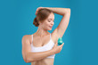 © New Africa - Young woman applying deodorant to armpit on teal background