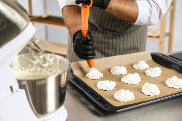 Wall Mural - Pastry chef preparing meringues at table in kitchen, closeup