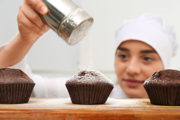 Wall Mural - Female pastry chef sprinkling cupcakes with sugar powder in kitchen