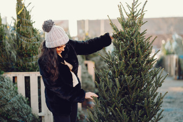 Elegant girl buys a Christmas tree. Woman in a fur coat. Beautiful lady with dark hair.