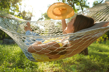 Poster - Young woman with hat resting in comfortable hammock at green garden