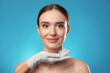 Poster - Doctor examining woman's face before plastic surgery on light blue background