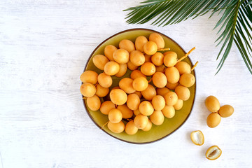 Wall Mural - Fresh raw yellow dates in plate with palm leaf on white wooden background. Top view	