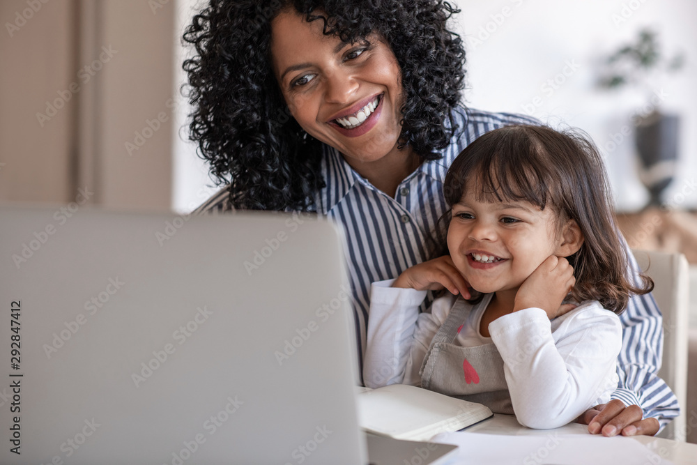 Busy mother and entrepreneur using a laptop with her daughter - obrazy, fototapety, plakaty 