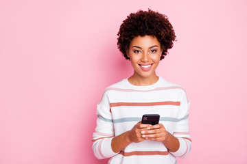 Wall Mural - Photo of pretty dark skin curly lady holding telephone addicted to internet reposts and comments wear white striped pullover isolated pastel pink color background