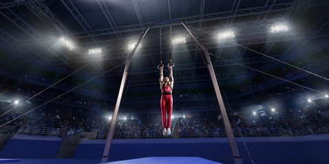 Wall Mural - Male athlete doing a complicated exciting trick on gymnastics rings in a professional gym. Man perform stunt in bright sports clothes