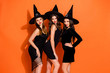 © deagreez - Photo of cruel witch ladies ready for halloween student event wear tempting black dresses and hats isolated orange color background