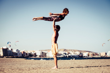 couple of two adults in relationship or friendship doing acro yoga together - man holding with his arms a woman while she's doing some posture