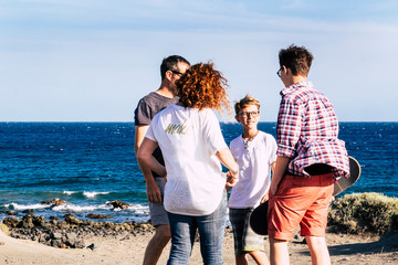 happy family together and hugged at the beach n front and looking at the sea - four persons - child and teenager - millennial with skate board in his arm