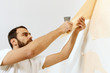 © Dmitrii Kotin - Man in with a scraper in the process of removing old wallpaper.