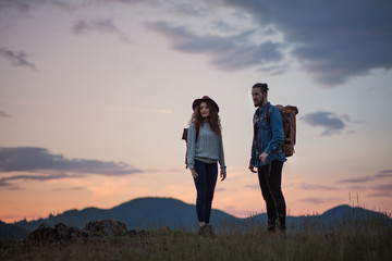 Wall Mural - young tourist couple travellers with backpacks hiking in nature at dusk.