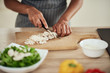 © nenadaksic - Close up of mixed race woman in apron standing in kitchen and chopping mushrooms.
