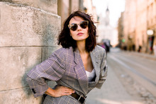 Trendy Fashion Woman In Jacket And Sunglasses Walking On The Street, Urban City Scene. Copy Space