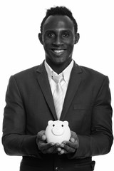 Young happy black African businessman smiling and holding piggy bank