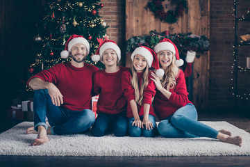 Happy holidays.Photo of dad mom sister brother spending x-mas eve together sitting floor near garland tree indoors wear santa caps and red sweaters