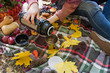 Autumn picnic in the park. Girl pours tea from a thermos into a cup. Basket with flowers on a blanket in yellow autumn leaves. . Autumn concep