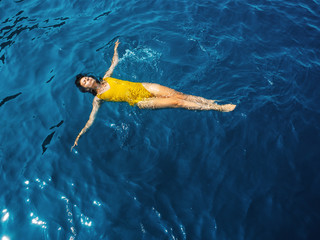 young woman in a one-piece yellow swimsuit floats on the surface of the water.