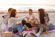 © Syda Productions - friendship, leisure and fast food concept - group of happy friends eating sandwiches or burgers at picnic on beach in summer