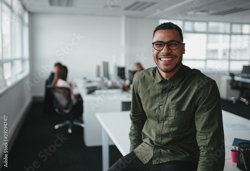 Cuadros en Lienzo Portrait of a successful smiling young professional businessman sitting over des