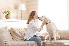 Young Pretty Woman In Casual Clothes Hugging Her Beloved Big White Dog Sitting On The Sofa In The Living Room Of Her Cozy Country House. Animal Communication Concept