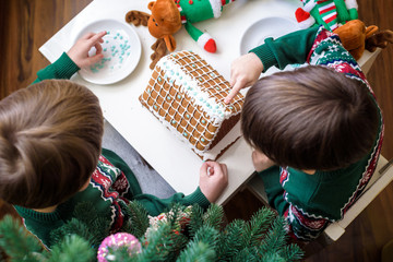 Two sweet boys, brothers, making gingerbread cookies house, decorating at home in front of the Christmas tree, child playing and enjoying, Christmas concept