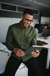 © StratfordProductions - Smiling young businessman working online on digital tablet while sitting on desk in a office