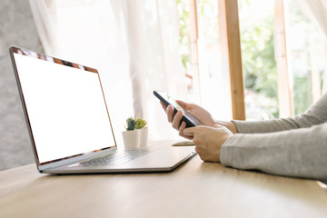 Wall Mural - Asian woman holding phone and using computer laptop on wooden table