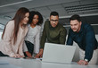© StratfordProductions - Group of concentrated diverse business team discussing information on laptop screen over the desk in office