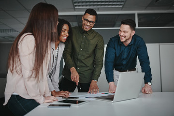 Wall Mural - Group of young multiracial business people standing together at the office desk discussing business strategy looking at laptop 