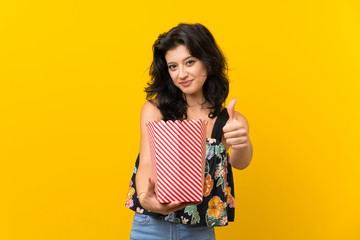 Young woman over isolated yellow background holding a bowl of popcorns