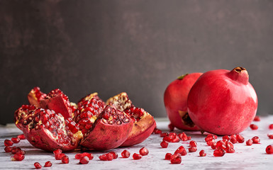 An open pomegranate, scattered grains and two whole pomegranates in the background. Light and dark background