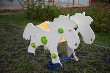 Swing on a spring in the form of white horses with green apples. Playgrounds, toys.