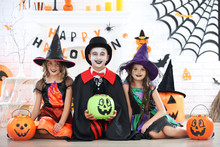 Young Two Girls And Boy In Halloween Costumes With Candies In Pumpkin Buckets