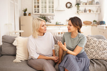 Two Caucasian Women Having Nice Lively Conversation In Living Room. Cute Young Woman Gesturing Emotionally, Proving Something While Talking To Her Middle Aged Mother On Sofa In Cozy Interior