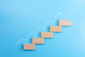 wooden block stacking as step stair with white arrow up on blue background, ladder of success in bus