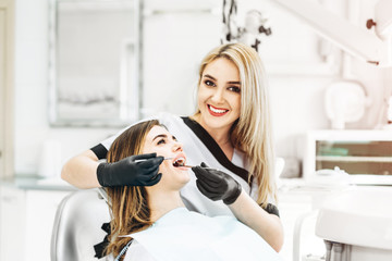 Wall Mural - Pretty young female dentist making examination and treatment for young female patient in dental clinic.