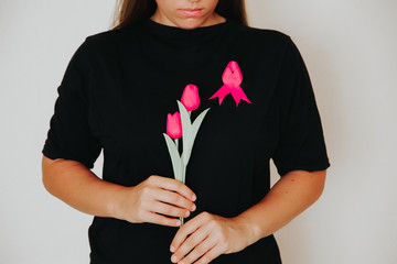 Wall Mural - Girl in black t-shirt with a symbol of breast cancer a pink ribbon on her chest holding pink tulips. Breast cancer concept.