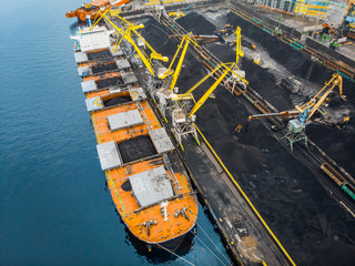 Wall Mural - Loading coal anthracite mining in port on cargo tanker ship with crane bucket of train. Aerial top view