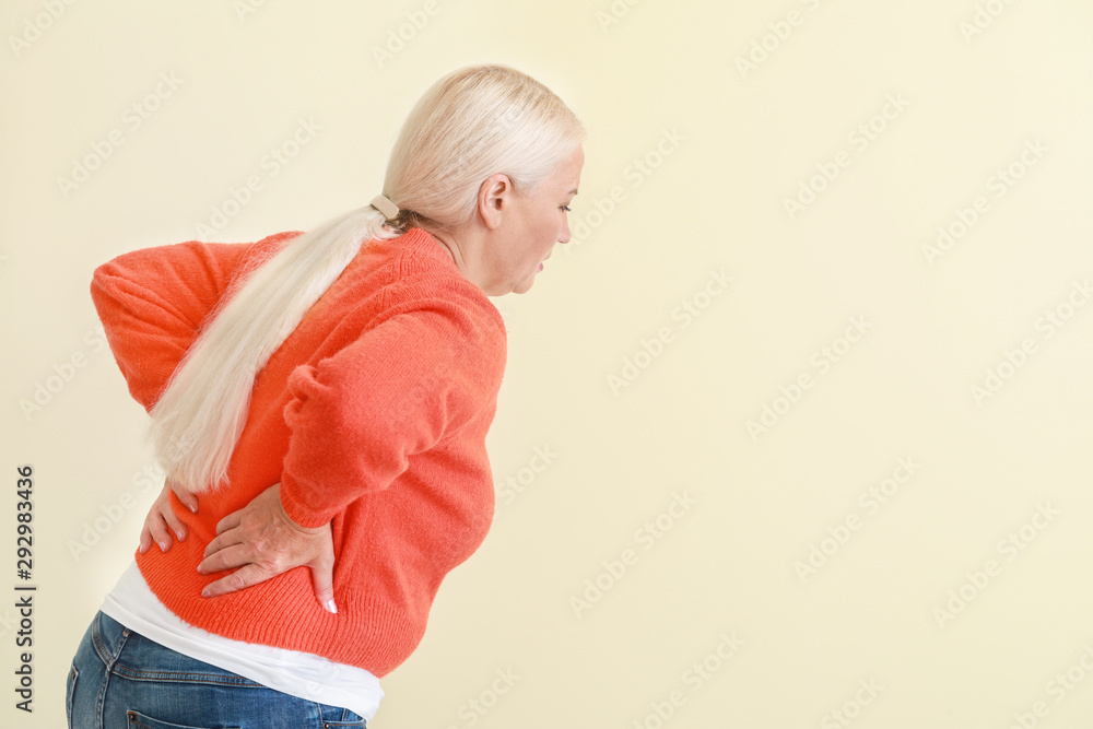 Mature woman suffering from back pain on light background
