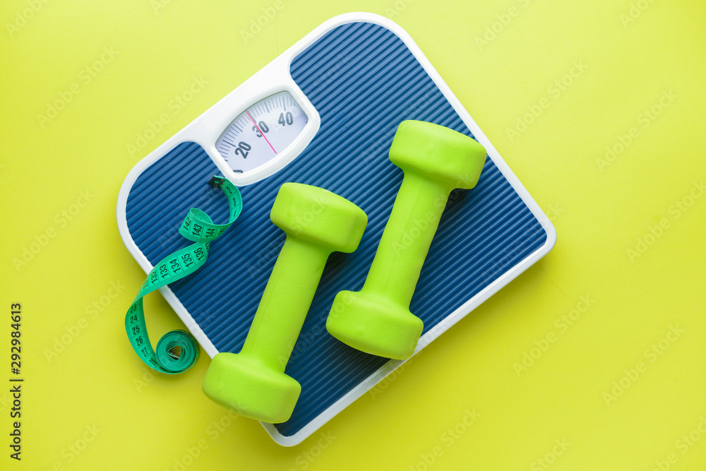 Scales, dumbbells and measuring tape on color background. Weight loss concept