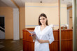 © Olha - Portrait of confident female doctor, with papers in hands, wearing white uniform. Preparing for a patient visit.