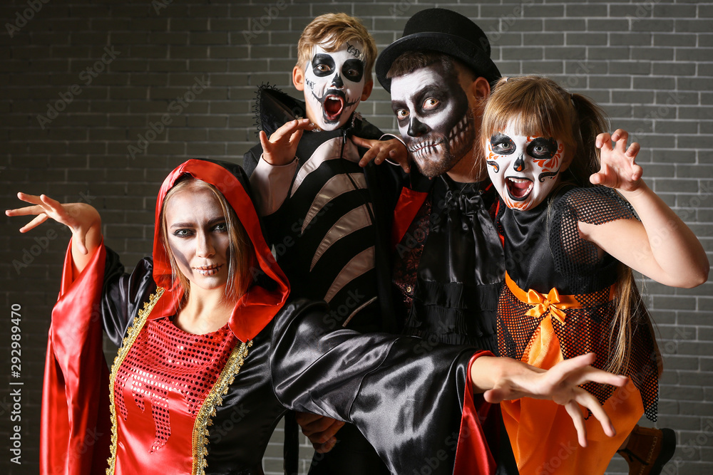 Family in Halloween costumes on brick background