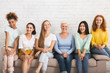Leinwandbild Motiv Smiling Diverse Women Sitting On Sofa Over White Brick Wall