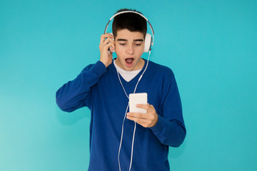 Wall Mural - young teenage man with mobile phone and trendy headphones isolated on color background