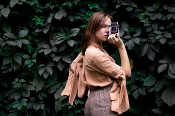 young girl photographer stands with a film camera near a wall of leaves in the forest, a woman photographs in nature