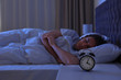 © New Africa - Alarm clock on nightstand near sleeping young man. Bedtime